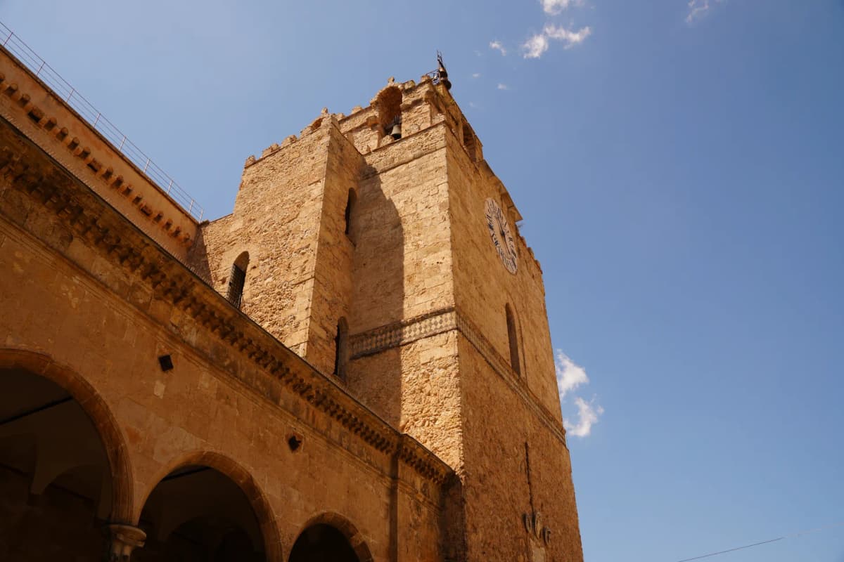 Wide-angle view of Monreale Cathedral's historic bell tower against a vivid blue sky in Sicily, Italy.